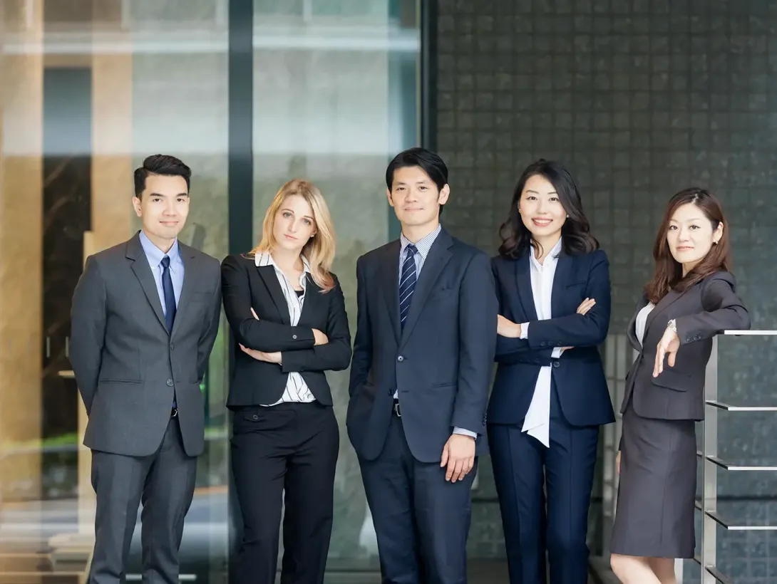 Five diverse business professionals in suits standing confidently outside a modern building.