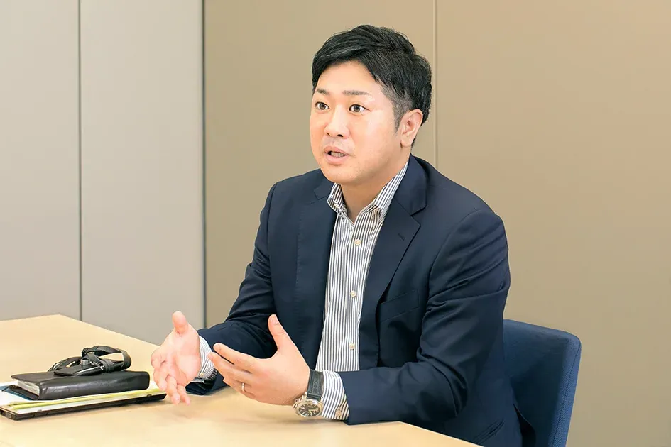 A male Honda employee seated at a table, gesturing with his hands while speaking.