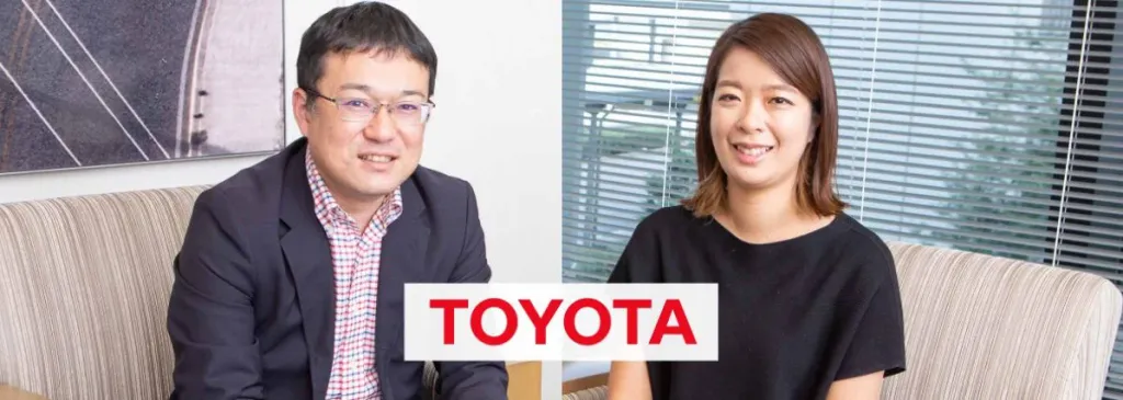 Two Toyota employees, a man and a woman, smiling during a business interview. Includes TOYOTA logo.